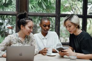 Three women of Asian and African ancestry meet with each other in an office.